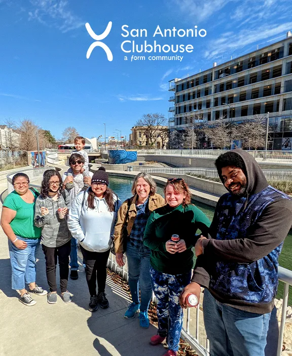 Un grupo sonriente de miembros de San Antonio Clubhouse reunidos al aire libre en un día soleado