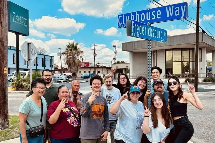 Miembros de San Antonio Clubhouse sonriendo juntos bajo el letrero de la calle Clubhouse Way