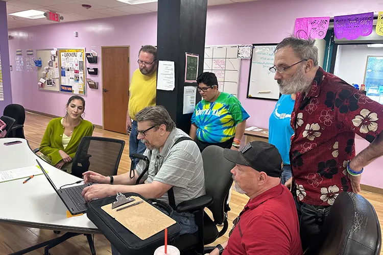 Members and staff gathered around a laptop at a table in the Clubhouse